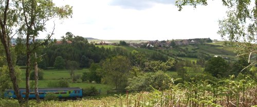 Train approaching Castleton station by Danby Park Wood, in the distance is Castleton Village on the ridge road south to Ralph Cross, Blakey Ridge and Hutton-le-Hole.