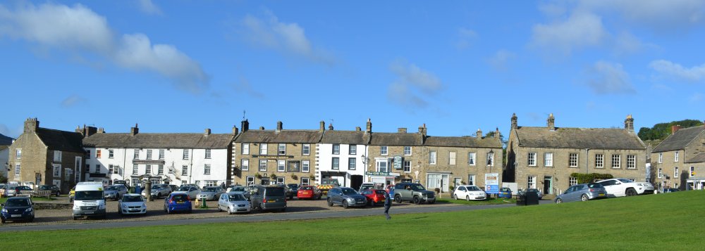 A broad view of the pubs, cafes and shops on the western side of the village green in Reeth North Yorkshire Dales National Park England