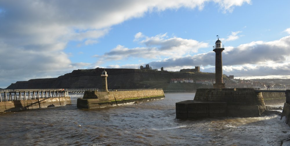 A very moody view from Whitby's west pier towards the harbour entrance lighthouse and St Mary's Church and Whitby Abbey ruins up on the East Cliff.
