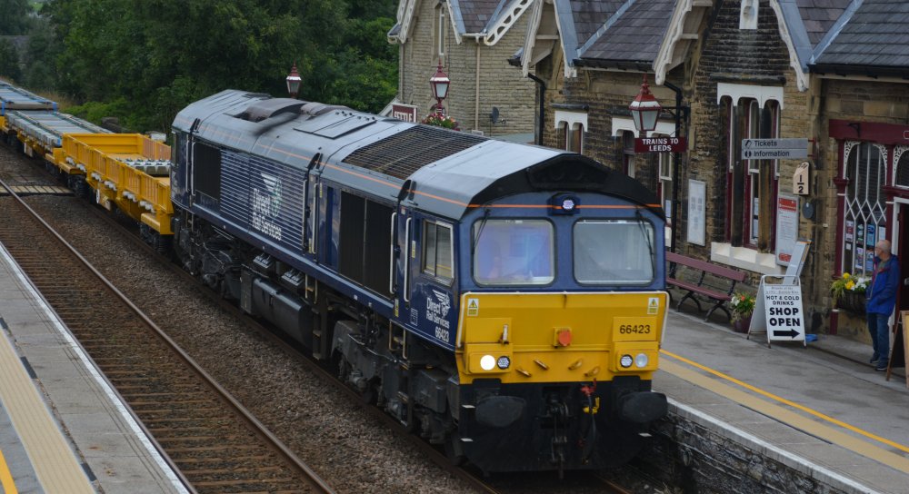 A DRS operated Class 66 diesel locomotive Class 66/4 66423 passing south through Settle station with a train of Network Rail wagons carrying concrete sleepers to Hunslet Tilcon GBRf Pendleton GBRf or Ashton-in-Makerfield Ks GBRF or Tuebrook Sidings GBRf ??? (July 2023)